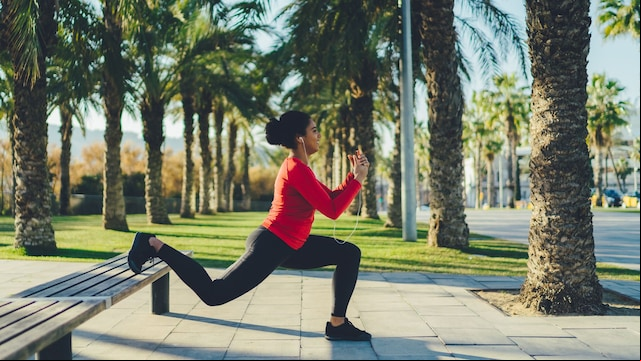 mujer haciendo lunges apoyada en un banco, al aire libre