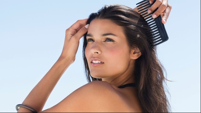 Mujer morena con bikini negro y pareo peinándose el cabello en la playa