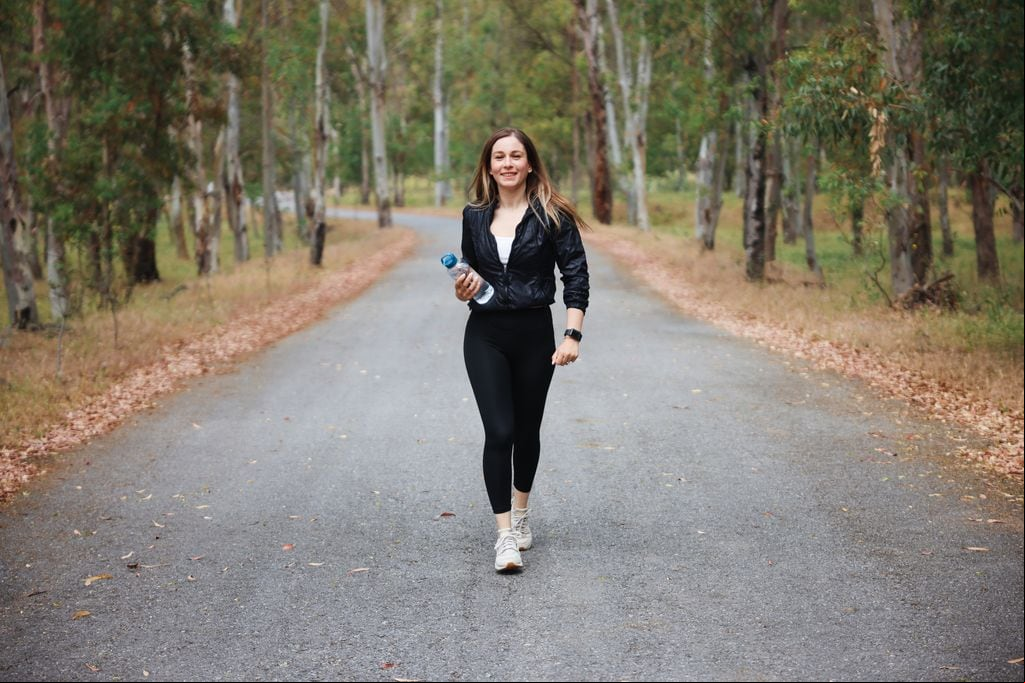 chica joven caminando por un parque con una botella de agua